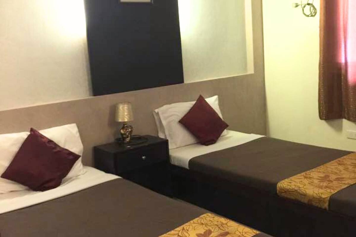 Une chambre d’hôtel avec deux lits simples, chacun étant équipé d’un oreiller et d’une table de chevet avec une lampe.