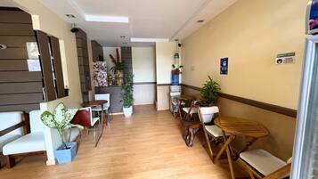 A hotel lobby with a wooden floor, white chairs, a wooden table, and potted plants.
