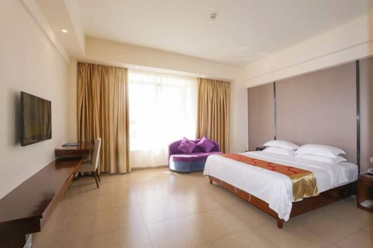 Une chambre d’hôtel avec un lit, un bureau, une chaise, un canapé et une grande fenêtre avec des rideaux.