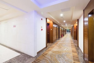 Un pasillo de hotel con alfombra estampada, puertas a ambos lados y un techo con iluminación empotrada.