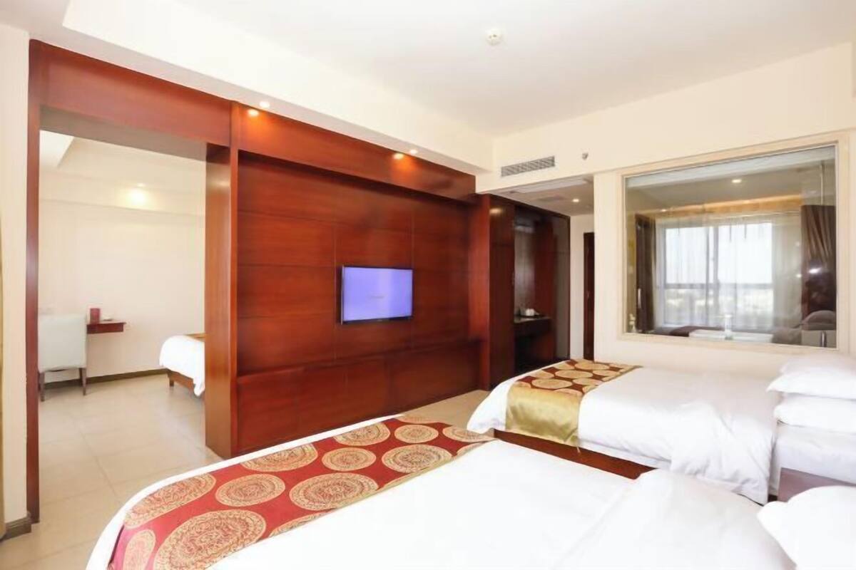 Une chambre d’hôtel avec deux lits, un téléviseur fixé au mur et une grande fenêtre.