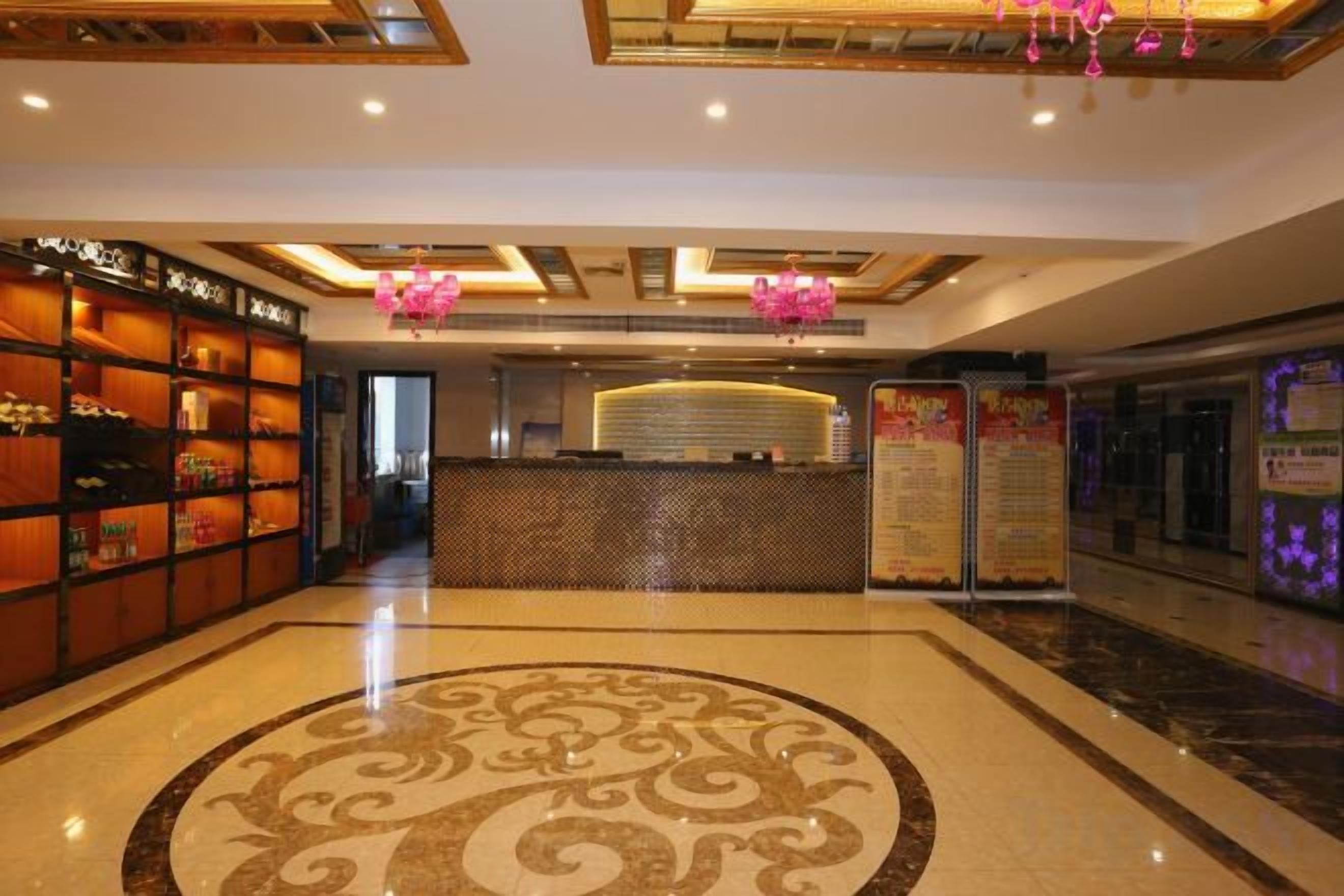 A hotel lobby with a reception desk, a patterned floor, and a ceiling with recessed lighting.