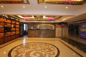 A hotel lobby with a reception desk, a patterned floor, and a ceiling with recessed lighting.