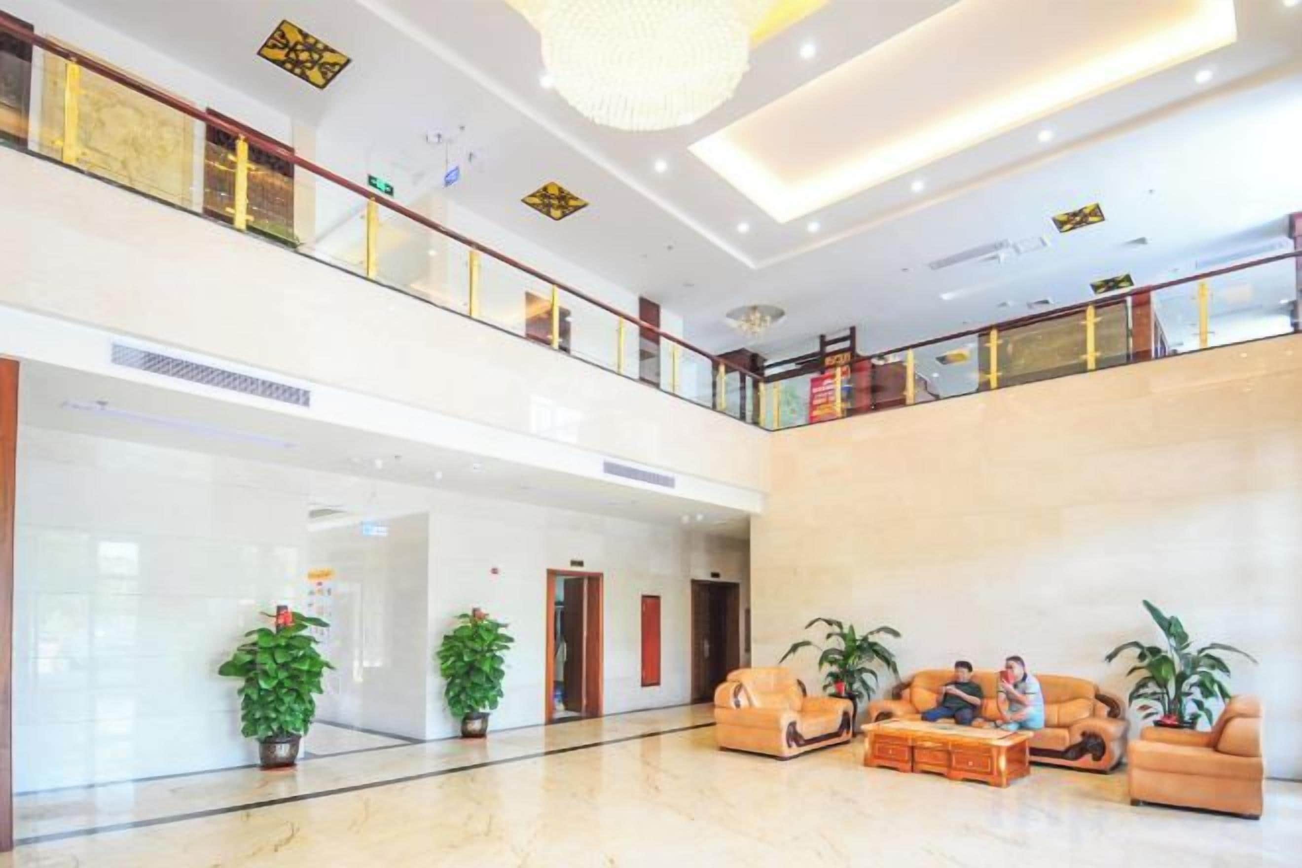 Eine geräumige Lobby mit hoher Decke, einem Balkon im zweiten Stock und einer Sitzecke mit Sofas und Topfpflanzen.