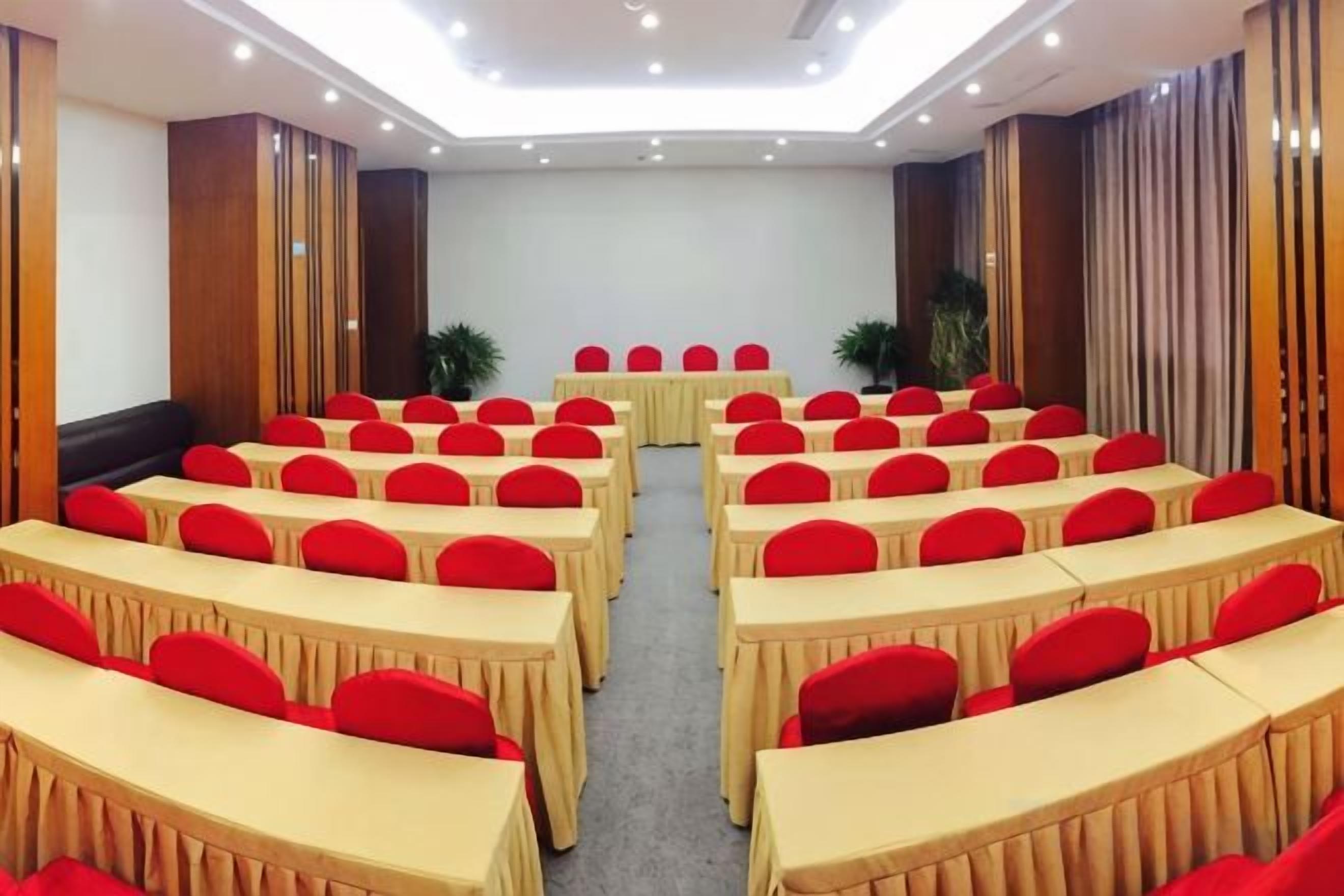 A conference room with rows of tables and chairs, a podium, and a large screen.
