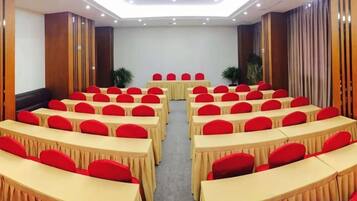 A conference room with rows of tables and chairs, a podium, and a large screen.