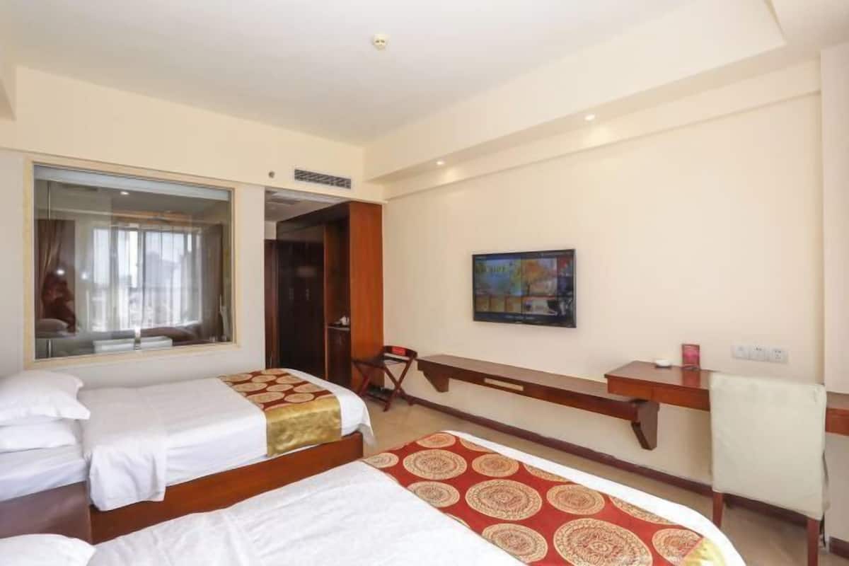 Une chambre d’hôtel avec deux lits, un bureau, une chaise, une fenêtre et un tableau au mur.
