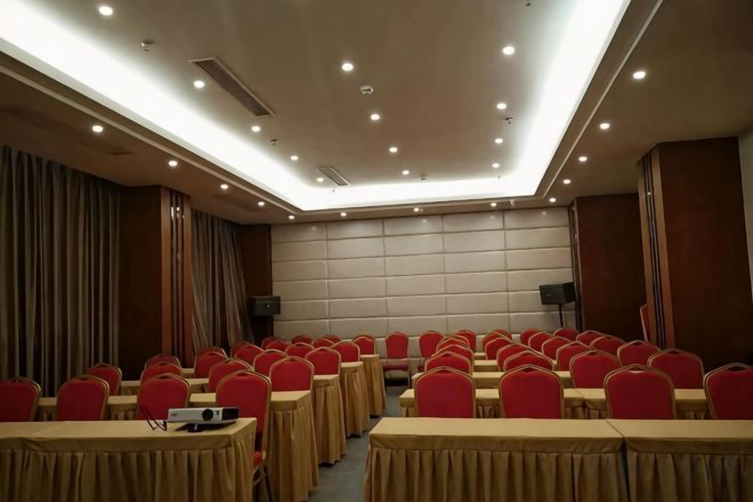A conference room with rows of tables and chairs, a stage, and a large screen.