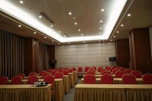 Une salle de conférence avec des rangées de tables et de chaises, une scène et un grand écran.
