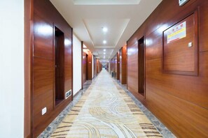 A hotel corridor with wooden paneling, a patterned carpet, and doors leading to rooms.
