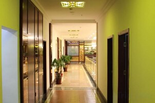 Un pasillo de hotel con suelo de baldosas, plantas en macetas y puertas que dan a las habitaciones.