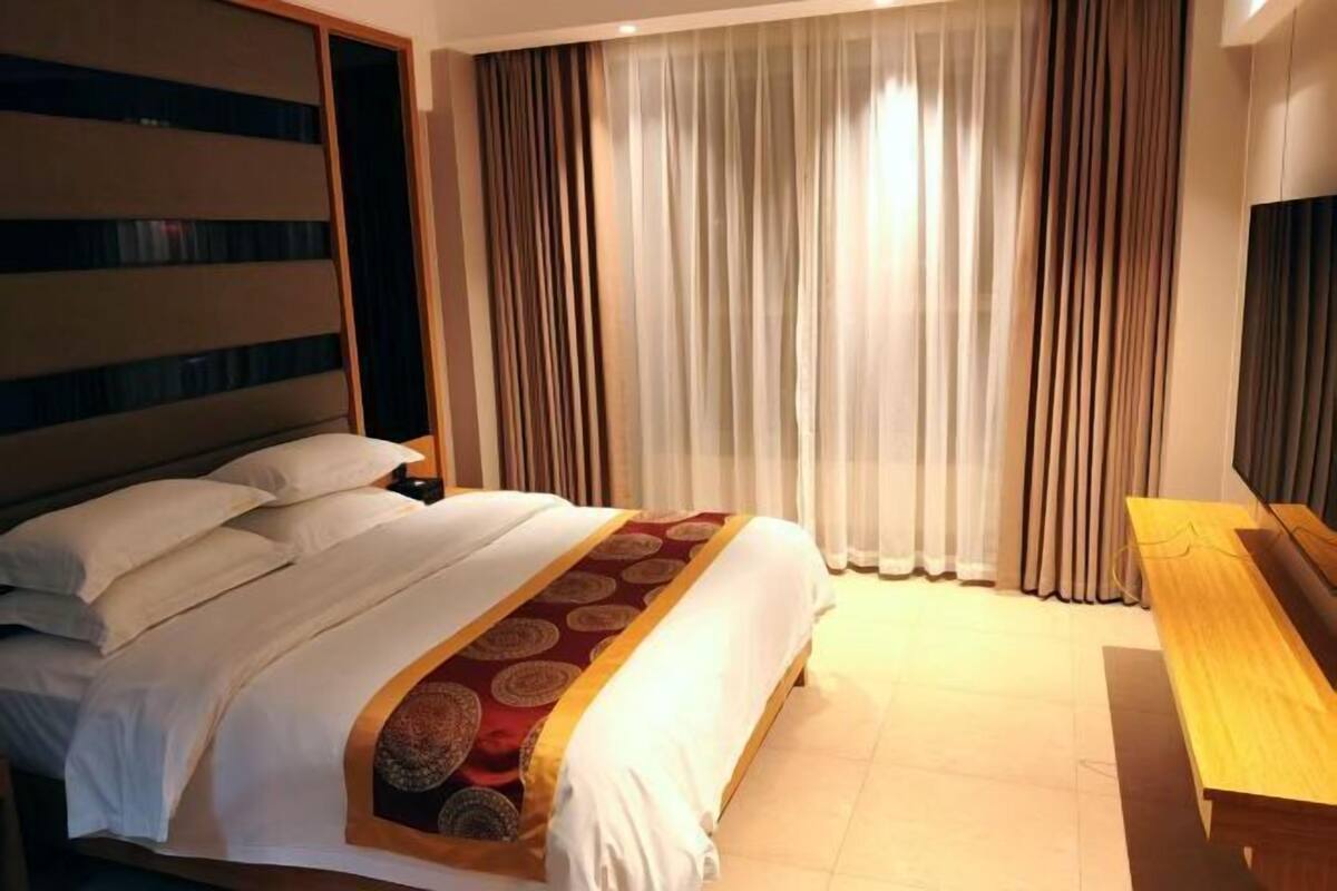Une chambre d’hôtel avec un grand lit, une tête de lit en bois, une télévision et un banc en bois.