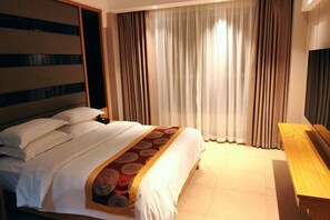 Een hotelkamer met een groot bed, een houten hoofdbord, een televisie en een houten bankje.