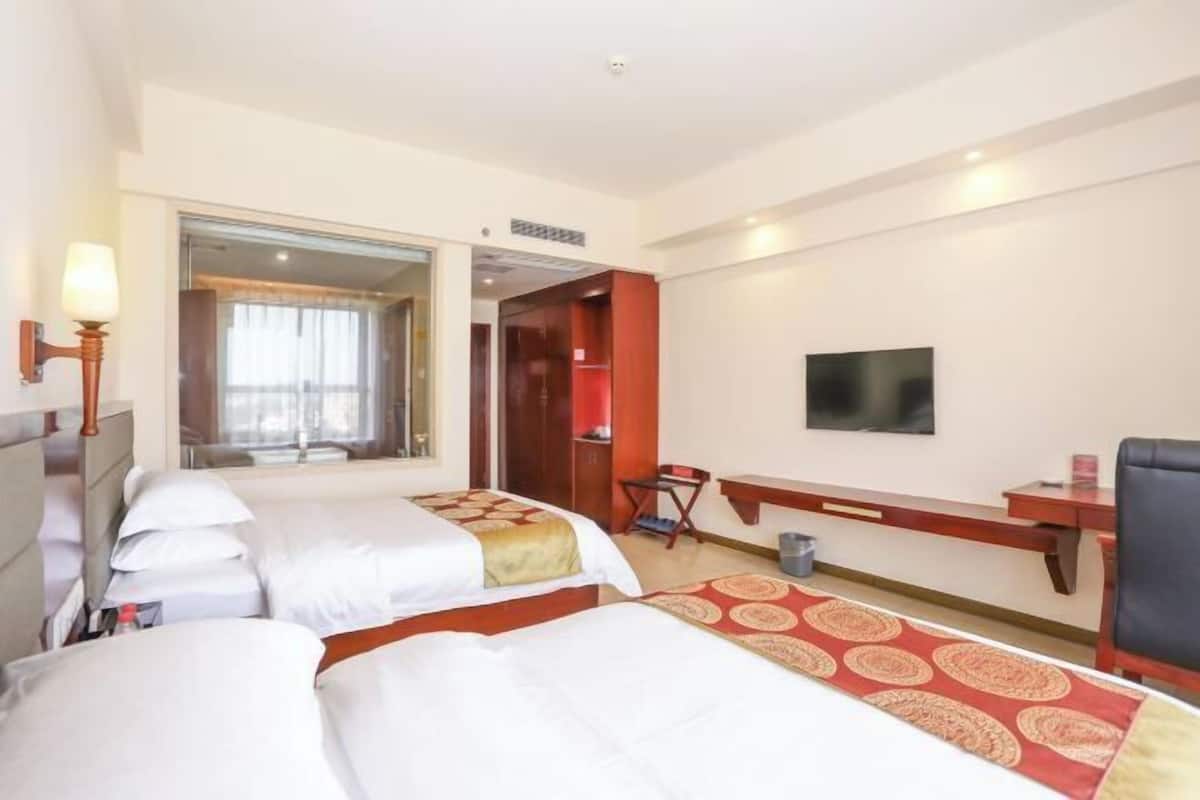 Une chambre d’hôtel avec deux lits, un bureau, une chaise, une télévision et une salle de bain visible à travers une porte ouverte.