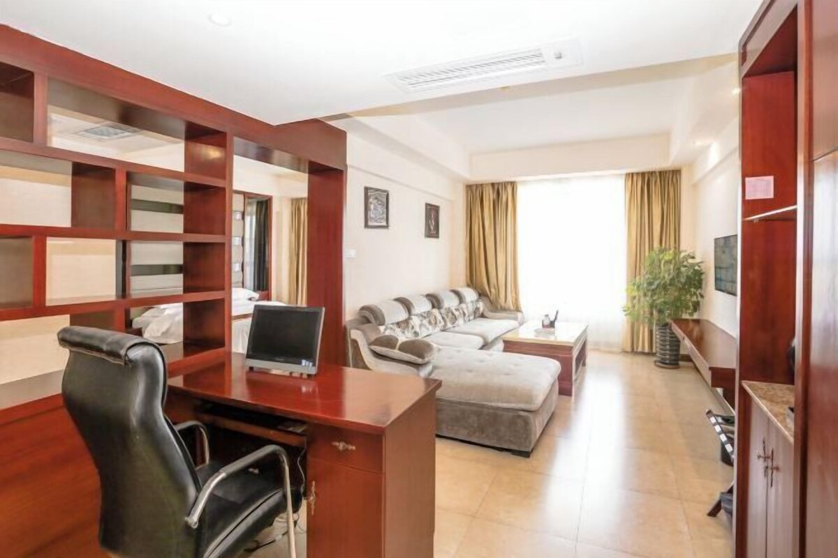 A hotel room with a wooden desk, a black office chair, a sofa, and a television.
