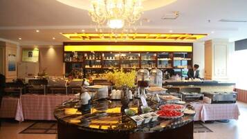 A hotel lobby with a central buffet table, a chandelier, and a bar area with shelves of bottles.