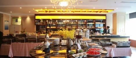 A hotel lobby with a central buffet table, a chandelier, and a bar area with shelves of bottles.
