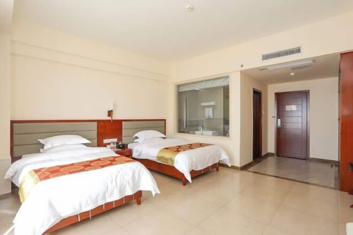 Une chambre d’hôtel avec deux lits, une grande fenêtre et une porte donnant sur une autre pièce.