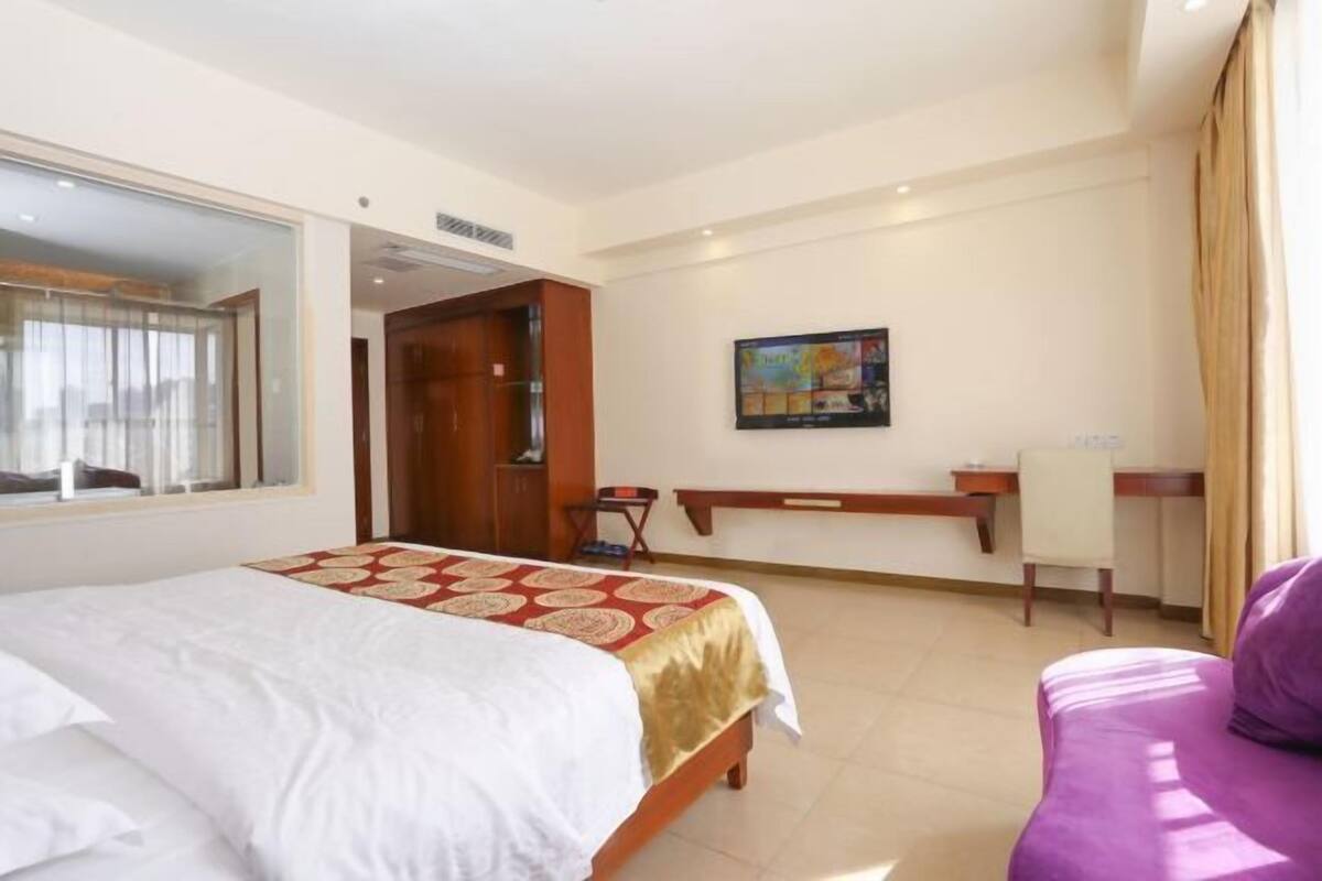 Une chambre d’hôtel avec un lit, un bureau, une chaise et un canapé violet.