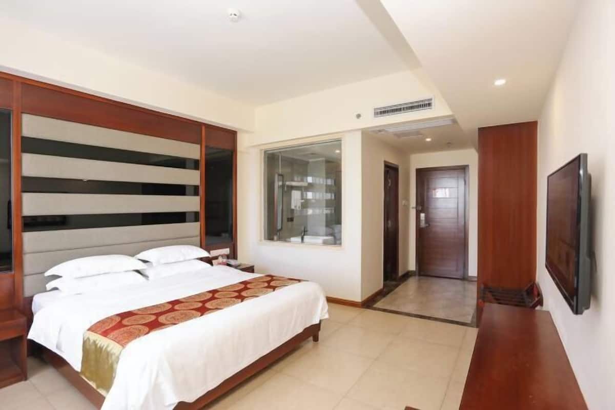 Une chambre d’hôtel avec un lit, une télévision, une grande fenêtre et une porte donnant sur une autre pièce.