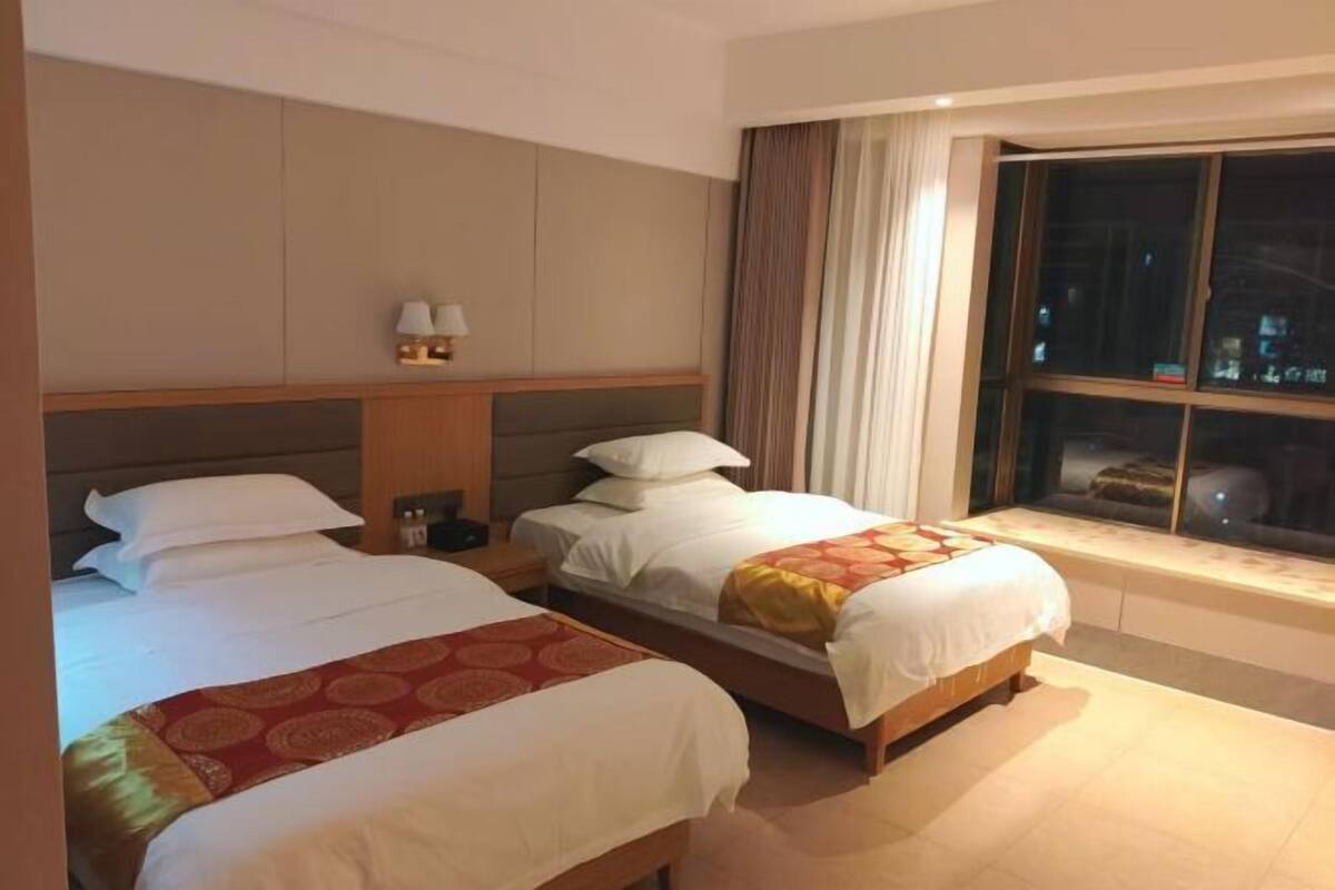 Une chambre d’hôtel avec deux lits, une table de chevet, une lampe et une fenêtre avec des rideaux.