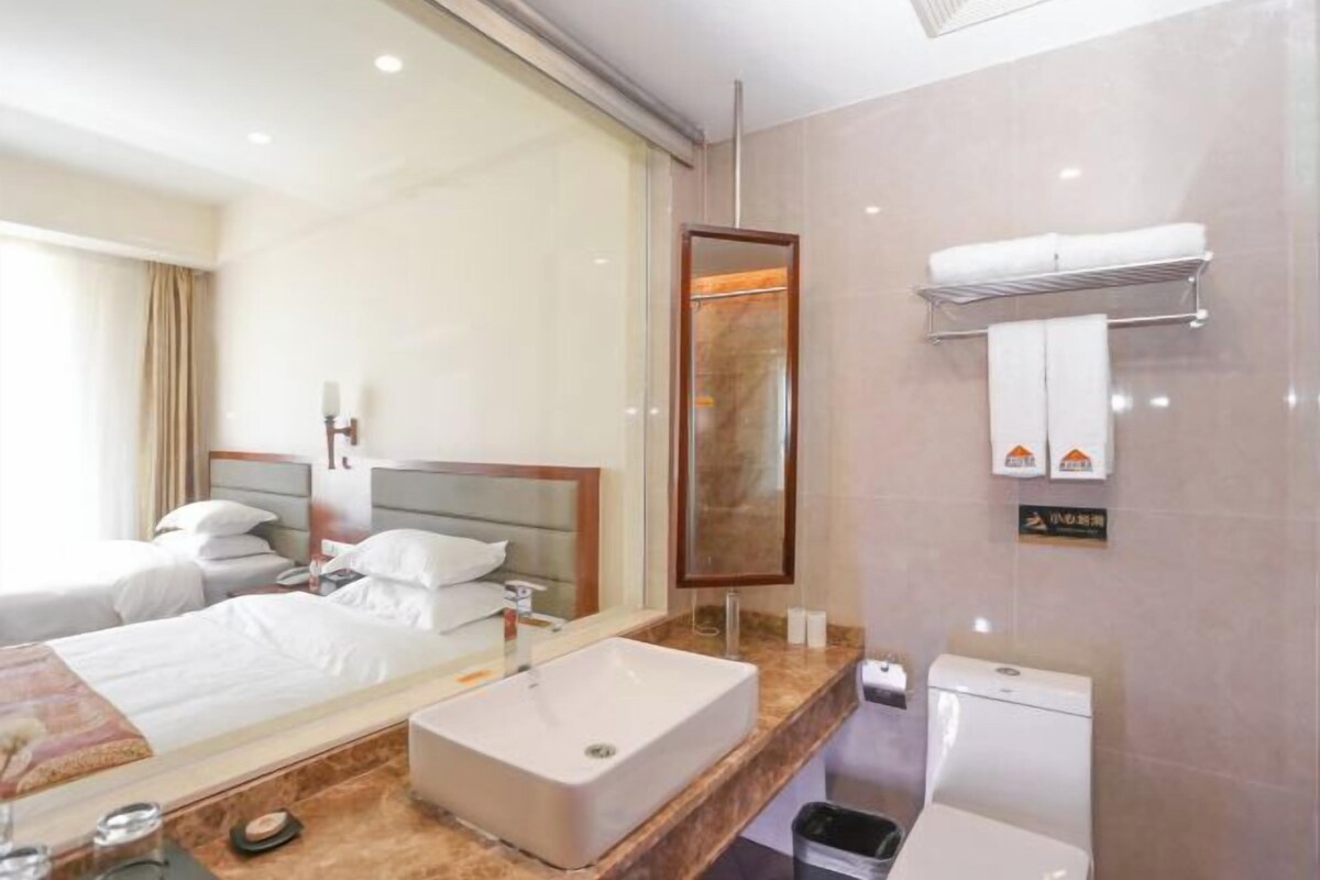A hotel room with a large mirror, a sink, a toilet, and two beds.