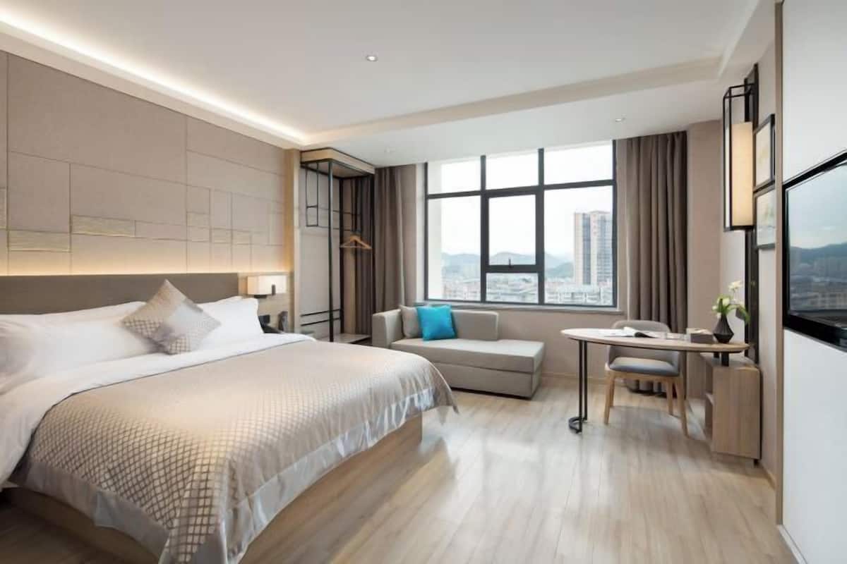 A modern hotel room with a large bed, a sofa, a desk, and a city view.