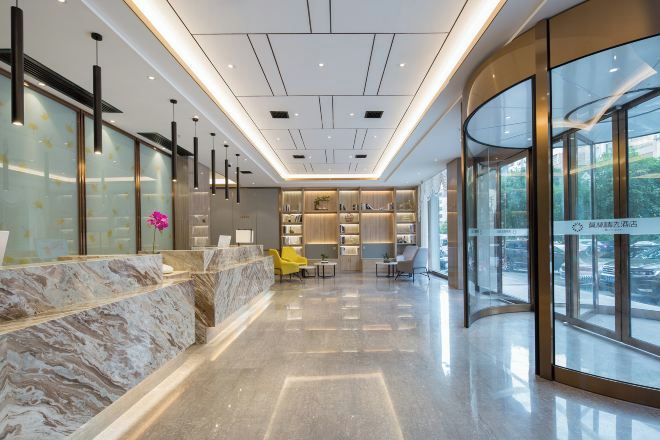 Un moderno vestíbulo de hotel con un mostrador de recepción de mármol, zona de estar y grandes ventanales.
