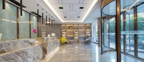 A modern hotel lobby with a marble reception desk, seating area, and large windows.