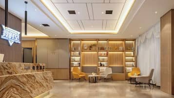 A hotel lobby with a reception desk, seating area, and a wall with shelves.