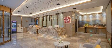A hotel lobby with a reception desk, seating area, and a digital kiosk.