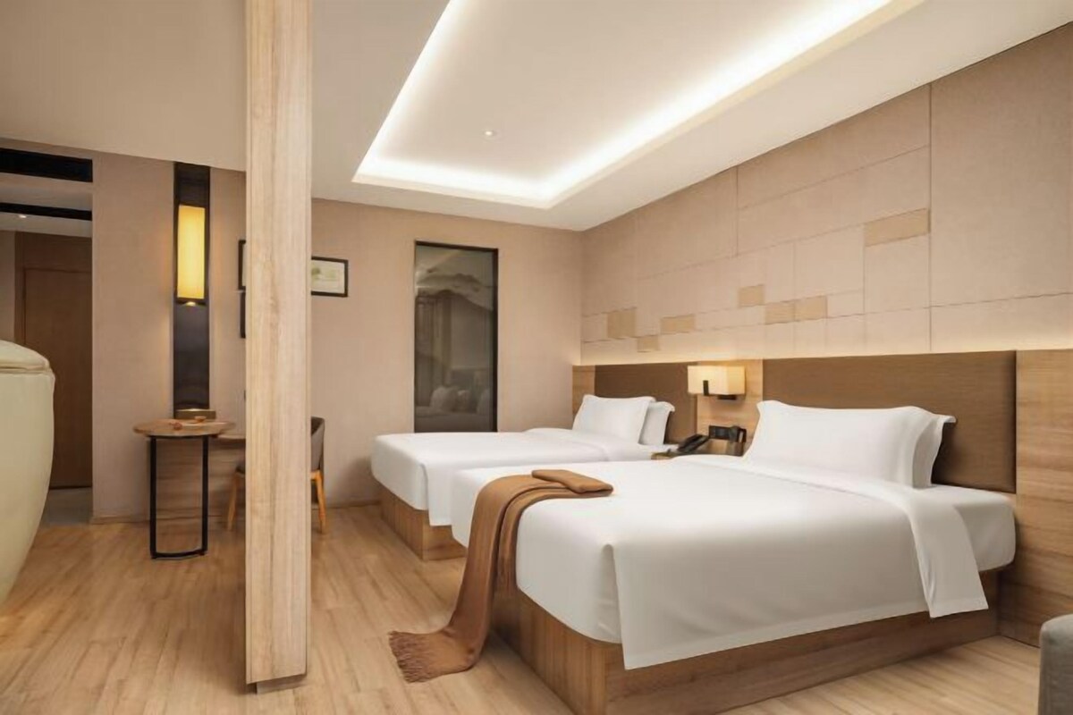 A hotel room with two beds, a wooden floor, a large window, and a modern design.