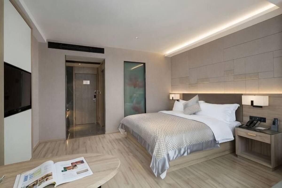 A modern hotel room with a bed, bedside table, lamp, and a door leading to a bathroom.