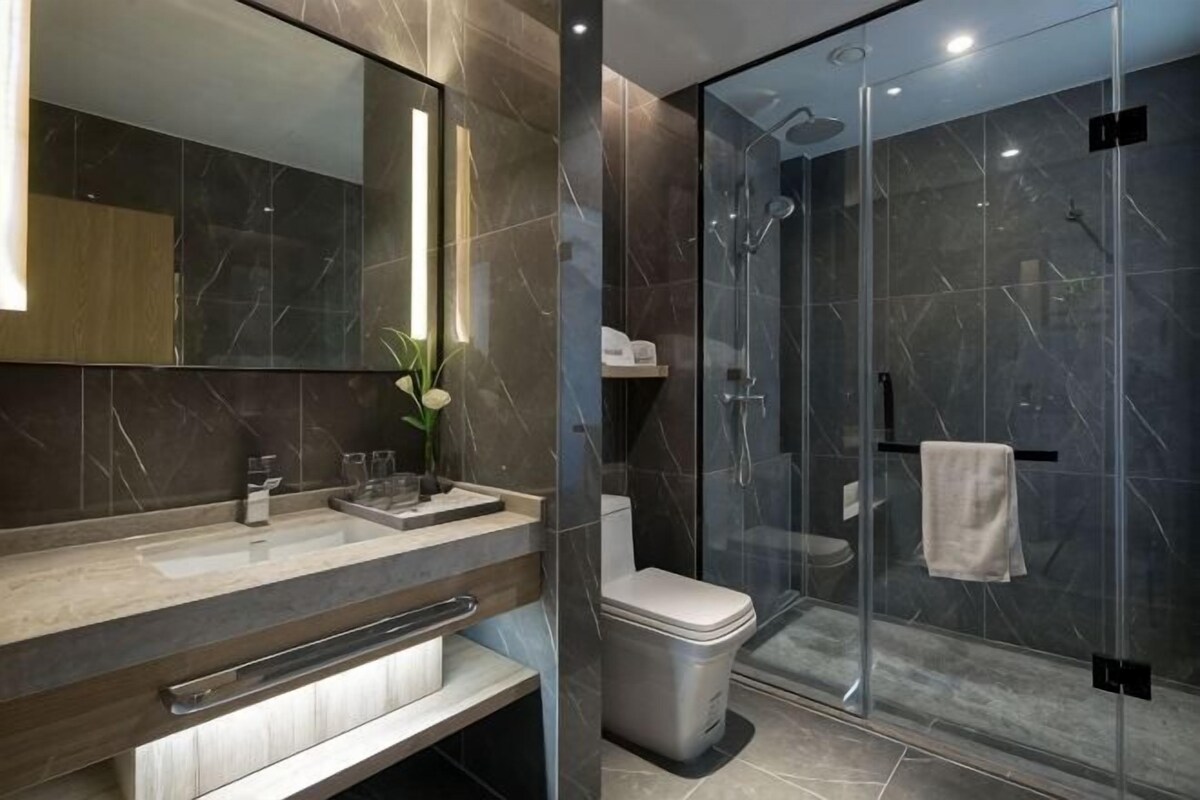 Une salle de bain moderne avec une douche à parois de verre, un mur recouvert de carreaux de marbre et un meuble-lavabo avec un miroir.