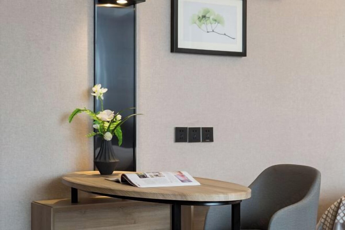 Une pièce moderne avec une table ronde en bois, une chaise sombre, un vase avec des fleurs blanches et un tableau encadré accroché au mur.