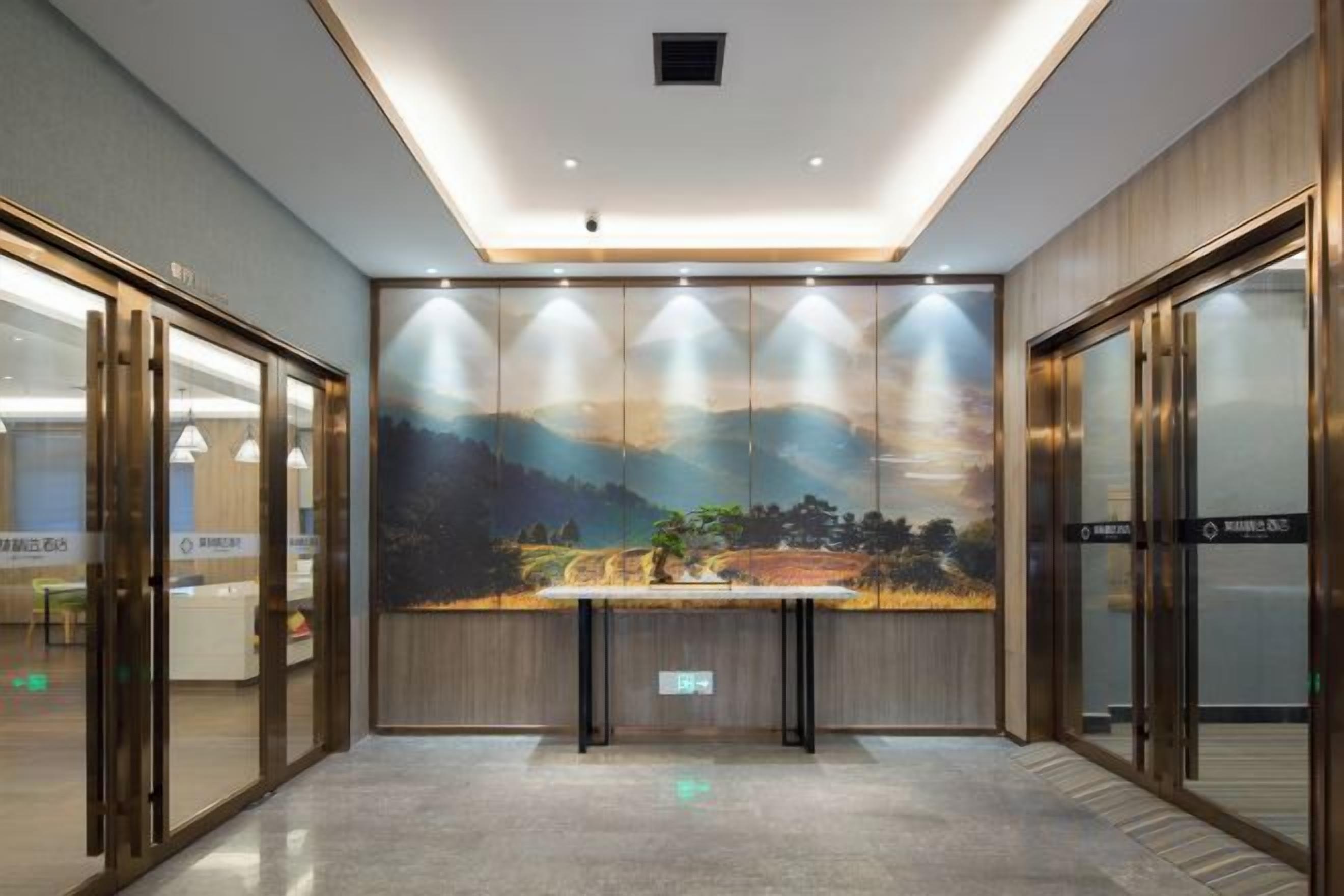 A hotel lobby with a reception desk, glass doors, and a mural of a landscape.