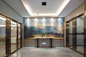 Un hall d’hôtel avec un comptoir d’accueil, des portes vitrées et une fresque représentant un paysage.