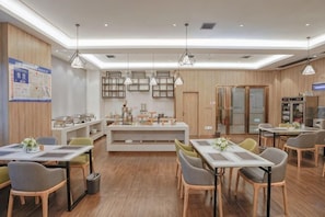 A modern restaurant with wooden flooring, pendant lighting, and a central island. Tables are arranged around the island, and there are chairs and a trash bin visible. - Molin Collection Hotel (Liuyang Haoting) (Liuyang)