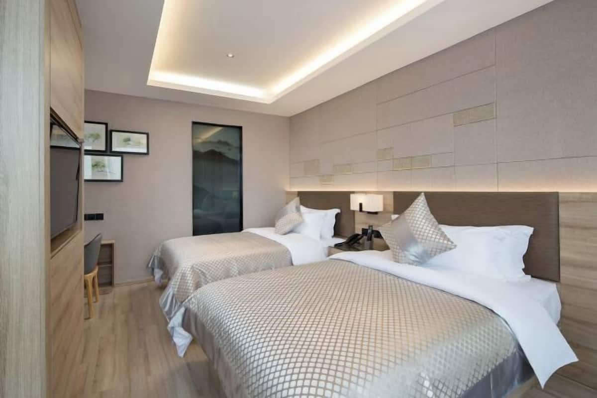A hotel room with two beds, a desk, and a large window.