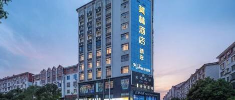A multi-story hotel with a prominent vertical sign, a ground-level entrance, and a street view with other buildings.