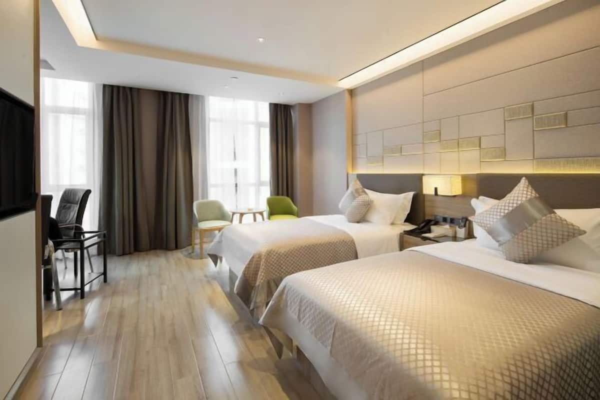 A hotel room with two beds, a desk, a chair, and a TV.