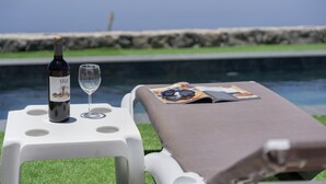 A poolside setting with a bottle of wine, a glass, and a magazine on a lounge chair. - Luxury House 'La Cueva del Guanche' with Sea Views, Private Pool & Wi-Fi (Adeje)