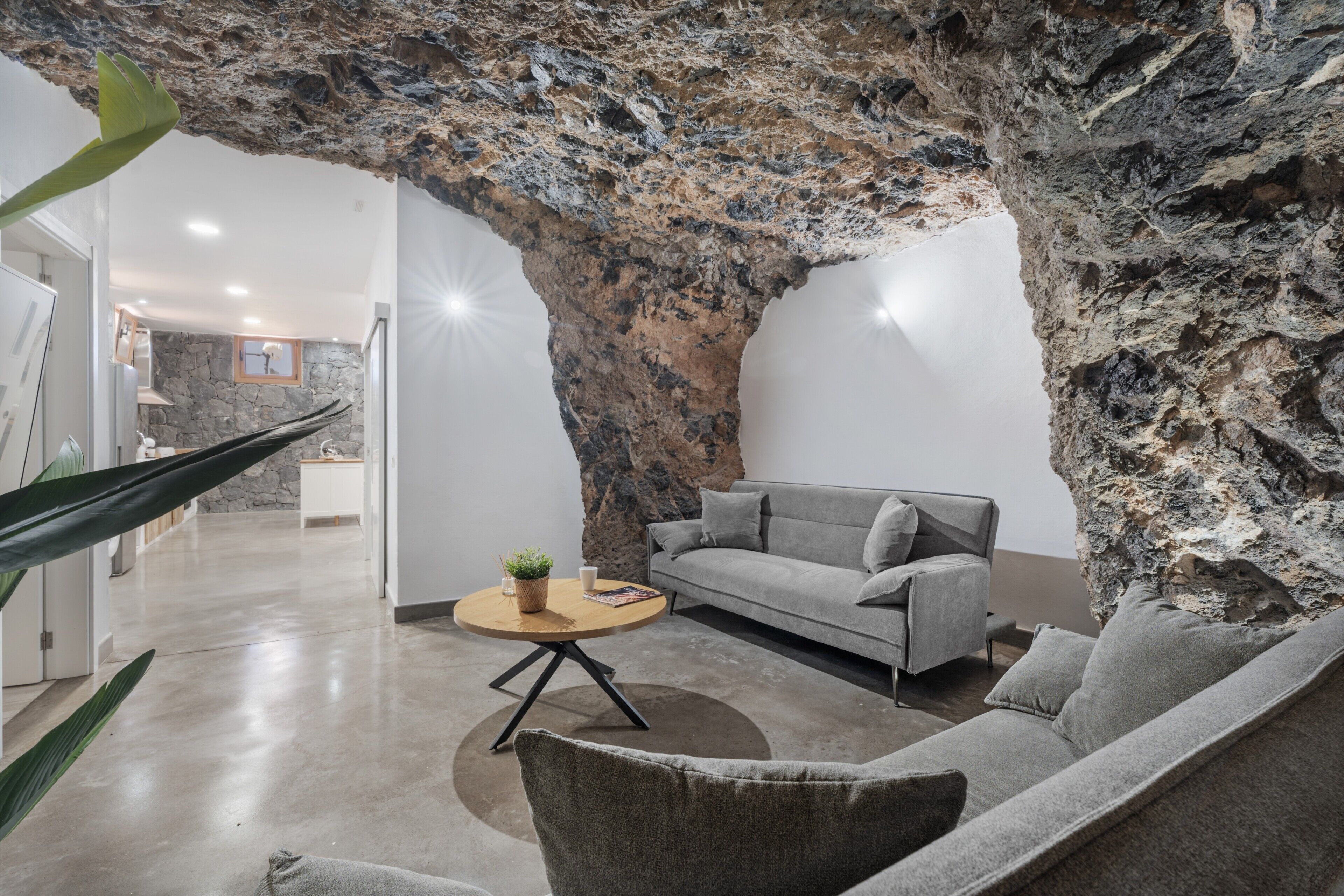 Una sala de estar moderna con un sofá gris, una mesa de centro redonda y una gran formación rocosa.