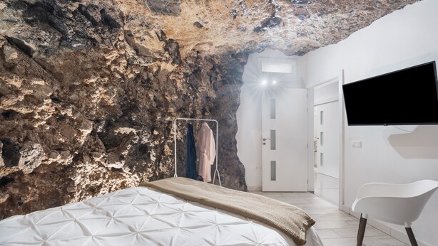 A bedroom with a bed, a TV, a chair, and a wardrobe. - Luxury House 'La Cueva del Guanche' with Sea Views, Private Pool & Wi-Fi (Adeje)