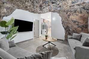 Un salon moderne avec un mur en pierre, un téléviseur à écran plat, une table basse ronde et un canapé gris.
