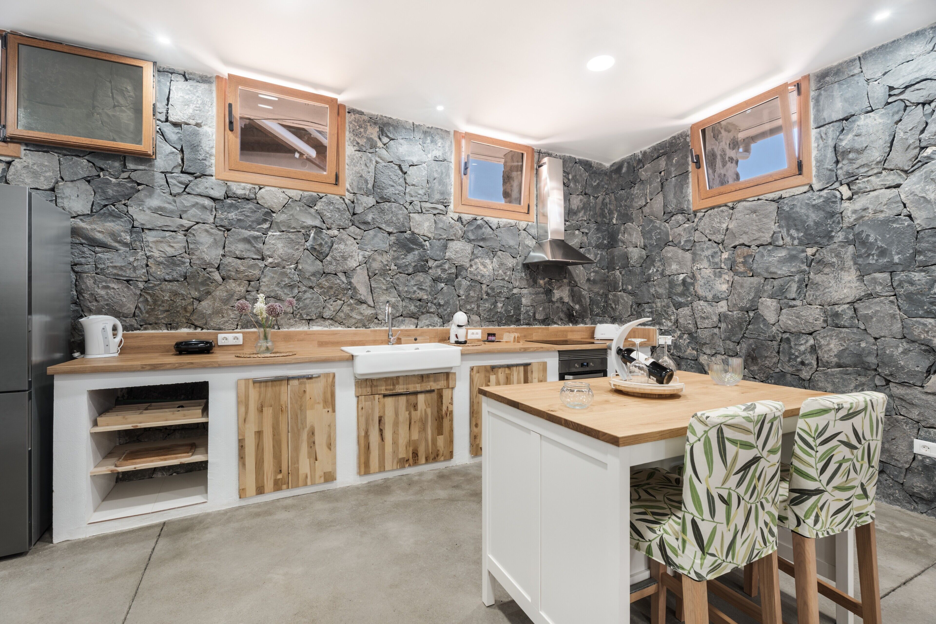 A kitchen with a stone wall, wooden cabinets, a built-in island, and a window.