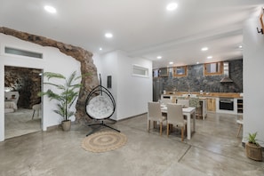 Une cuisine moderne agrémentée d’éléments en pierre, un coin repas avec une table ronde et un espace salon confortable avec un fauteuil suspendu.