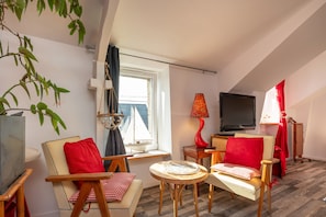 A cozy room with a TV, two chairs, a small table, a lamp, and a window with a view of sailboats. - Studio Apartment 'Dans Maison Proche Gare' with Shared Terrace, Shared Garden and Wi-Fi (Brech)