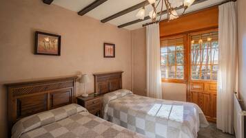 Une chambre à coucher avec deux lits, des têtes de lit en bois, un lustre, une fenêtre avec des rideaux et des tableaux encadrés accrochés au mur.