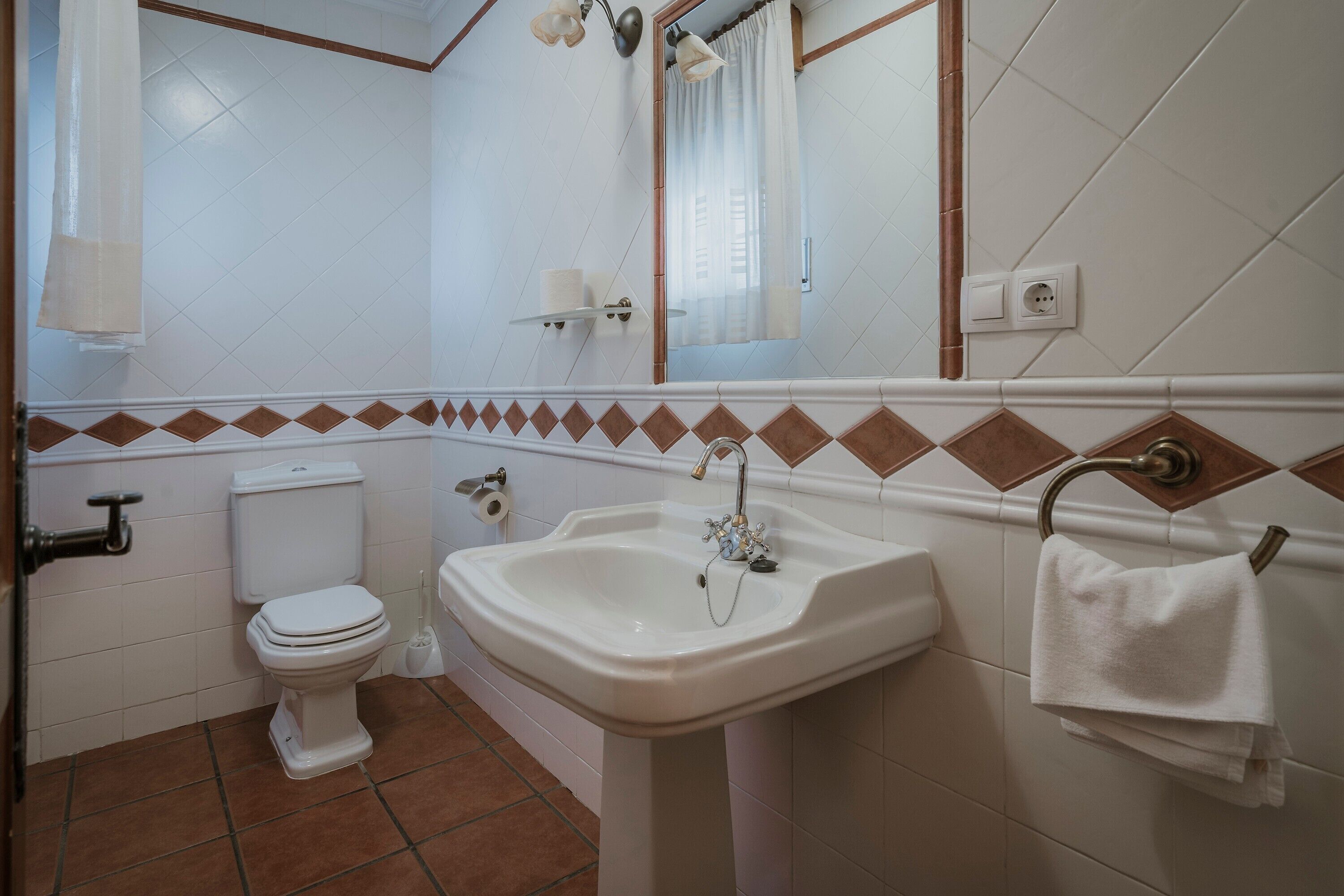 Ein Badezimmer mit Toilette, Waschbecken, Spiegel, Handtuchhalter und Fliesenwänden.